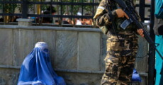 Afghanistan: una donna vestita con il burga seduta a terra controllata da un talibano.