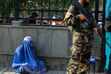 Afghanistan: una donna vestita con il burga seduta a terra controllata da un talibano.